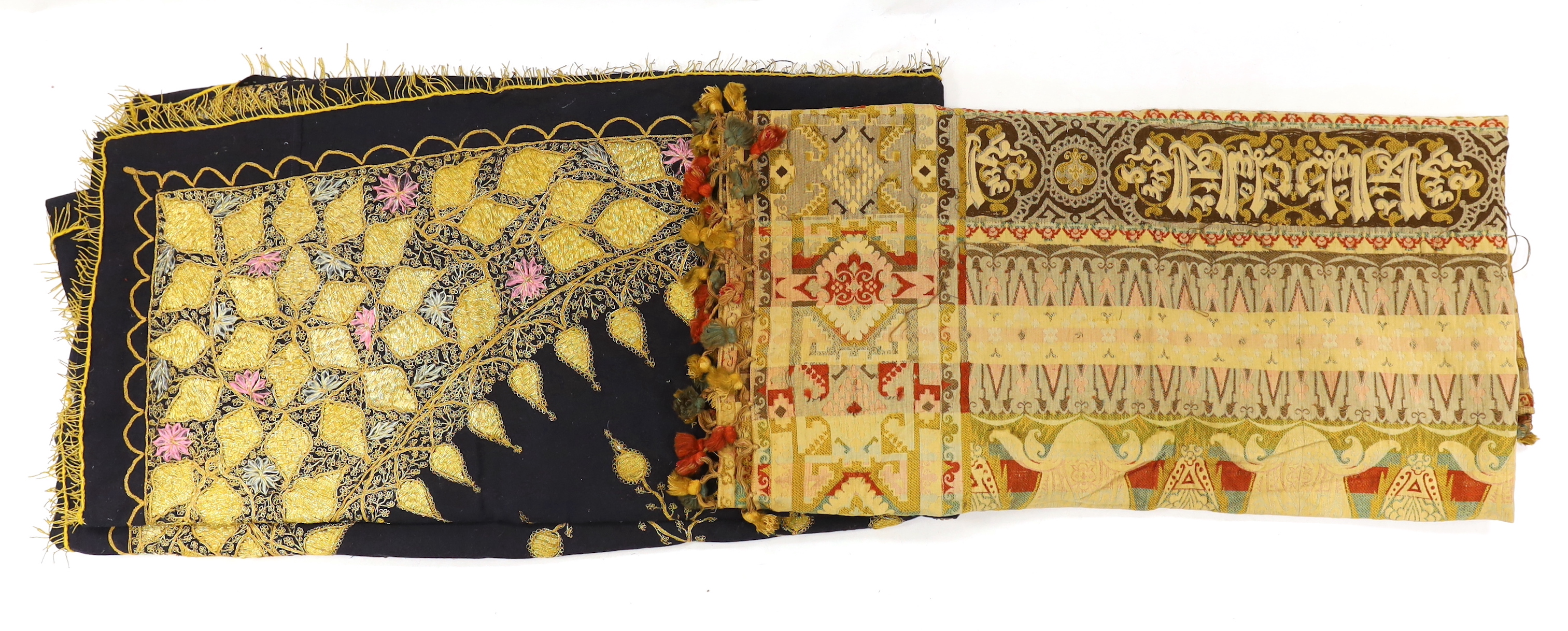 An Indian gold thread and coloured silk floss embroidered black wool cover with gold thread fringing and a later woven cover with bobble edging, black and gold cover 172cm x 169cm